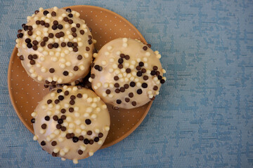 three round donuts in white glaze with chocolate balls stand on a brown polka dot plate on a blue texture background top view