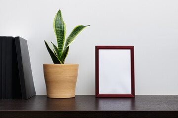 Brown wooden frame mockup in portrait orientation with a cactus in a pot and book  on dark workspace table and white background