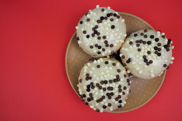 three round donuts in white glaze with chocolate balls stand on a brown polka dot plate on a red background top view