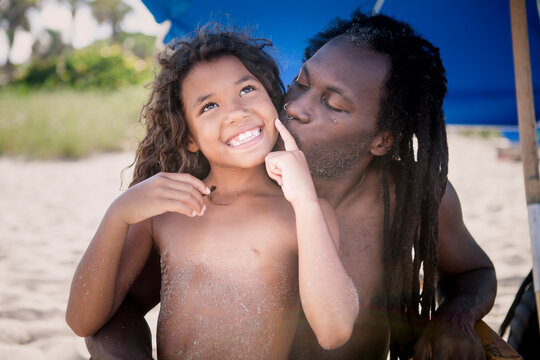 Father kissing shirtless cheerful daughter at beach