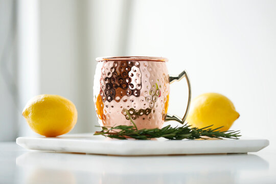 Close-up of drink in mug with lemons and rosemary in plate on table