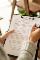 Hands of young female applicant with blue highlighter over contract on clipboard