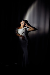 Side profile photo portrait of adorable woman in white dress posing in ray of light on dark studio background