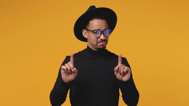 Confused young african american man 20s in black clothes hat eyeglasses isolated on yellow background studio. People lifestyle concept. Point fingers himself ask say who me no thanks i do not need it