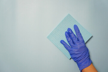 Close-up of a woman's hand in a blue glove holding a rag, a cleaning sponge, isolated on a blue...