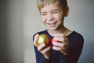 Cheerful boy with eyes closed holding Christmas Baubles against wall at home