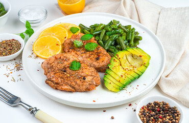 Delicious lunch with chicken steak and garnish with beans and avocado on a light background. Side view. Healthy, dietary food.
