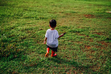 a happy kid walking on the grass wearing a red rubber boot carrying a magnifying glass