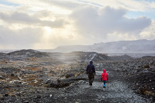 Rear view of father with daughter walking on mountain against cloudy sky during sunset