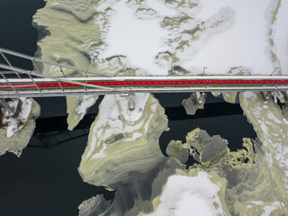 Red-green pedestrian bridge over the Dnieper river in Kiev. Snow patterns on the river. Aerial...