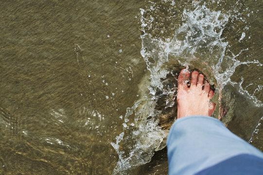 Low section of man stamping foot in water on shore