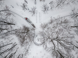 Red tractor removes snow in the park. Aerial drone view. Winter snowy morning.