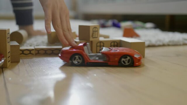 Tender hand playing with red car model on wooden blocks background.Retro car model on a wooden floor. Warm domestic interior. Childs leisure time