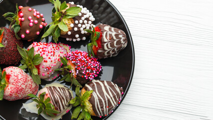 Chocolate covered strawberries. Strawberry in Chocolate decorated sprinkles. Colored sprinkle. Sweet delicious tasty dessert on black plate on natural white wooden table. Valentine's day 