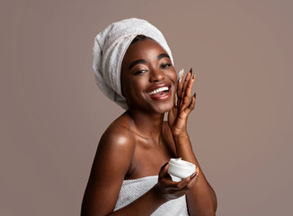 Beautiful young african american woman applying cream on face - obrazy, fototapety, plakaty