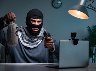 Terrorist burglar with gun working at computer