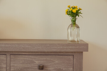 Interior decoration: bouquet of yellow wildflowers in a glass vase on gray wooden background