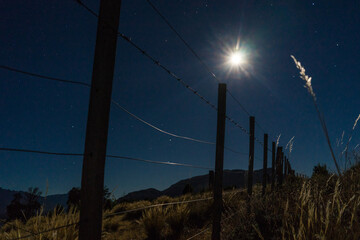 Low angle view of fence on grassy field against sky at night