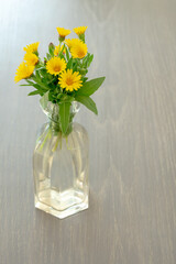 Interior decoration: bouquet of yellow wildflowers in a glass vase on gray wooden background