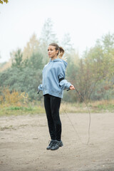 Blond active young woman in sportswear exercising with skipping-rope on path