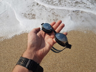 Close up male hand holding swimming glasses. He going to swimming in the sea, summer vacation concept.