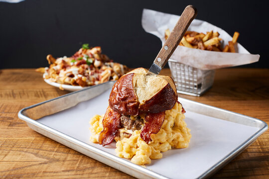 Close-up of macaroni burger with bacon and French fries served on wooden table