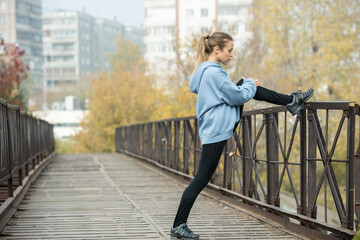 Girl standing on bridge with left leg bent in knee on fence and exercising
