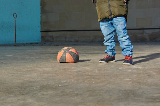 Boy with his hands in his pockets next to a deflated basketball ball.