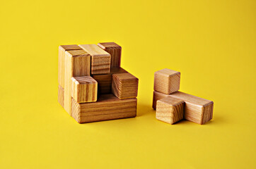 Logical game wooden cube puzzle the last element lies next to the yellow background close up. Solving logical problems. High quality photo