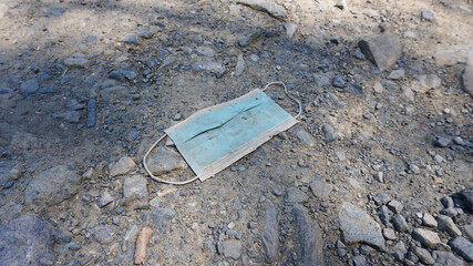 The medical mask is lying on the ground. An old used mask is lying dirty on the ground. People pollute the environment. Mask after coronavirus. Shadows from the trees fall on the ground and the mask.