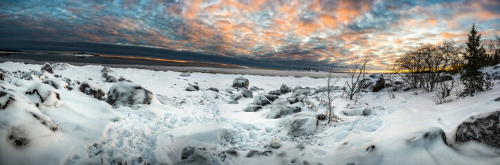 A tranquil panoramic landscape of cloud covered sky and snow covered half frozen lake with tourists in northern Europe with pine trees