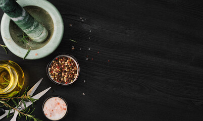 Layout of products for cooking seasoning in a marble mortar. Composition with sea salt, rosemary, olive oil and various types of pepper on a dark wooden background, top view with copy space