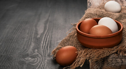 Chicken eggs close-up in a clay bowl on a burlap bed. Black wooden background with copy space for...