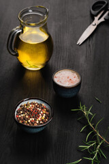 Closeup, selective focus on the products for cooking seasoning in a marble mortar. Composition with sea salt, rosemary, olive oil and various types of pepper on a dark wooden background