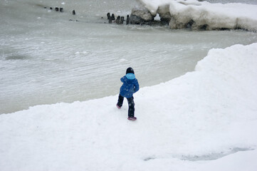 Fototapeta na wymiar child playing in snow, Winter landscape , Baltic Sea, snowy beach, ice breakwaters, cold water