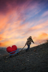 A determined child, despite the difficulties, pulls a stroller with a large plush heart up the hill...