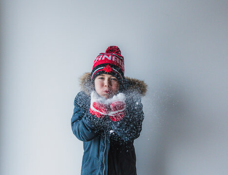Portrait of boy blowing snow while standing against white background