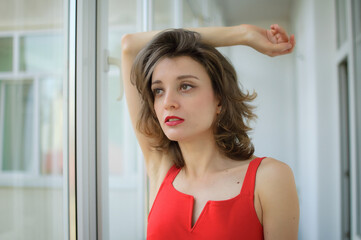 Young attractive woman in red clothes with sensual lips is possing at studio on window background