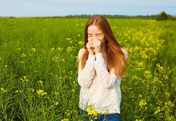 Allergic to pollen and flowering season, a redhead girl sneezing on a field