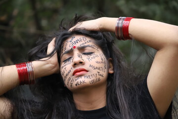 A southeast Asian brown woman protesting gender based violence by writing anti violence against women and girls messages all over her face and looking angry and sad