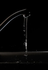 Naklejka na ściany i meble Leaking tap water against a black background 