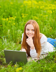 girl working in nature with a laptop lying on the green grass. The girl works as a freelance traveler.