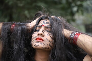 A southeast Asian brown woman protesting gender based violence by writing anti violence against women and girls messages all over her face and looking angry and sad