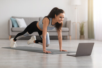 Active woman doing fitness at home, using laptop