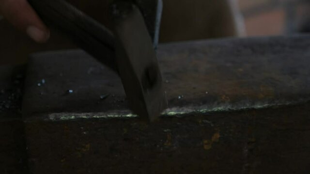 Blacksmith is hitting a red metallic stick with a hammer making something  
