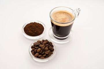 Black coffee in a glass cup and saucer with coffee beans around it

