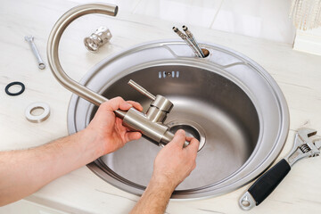 Close-up plumber hands holds a new faucet for installing into the kitchen sink, plumbing work or...