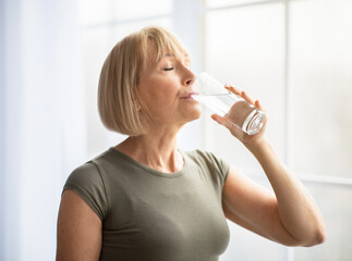 Fit senior woman drinking clear water during her workout break at home. Healthy lifestyle and wellness concept