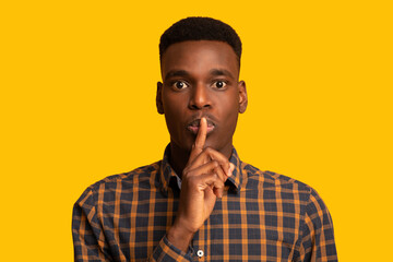 It's A Secret. Young Black Guy Making Silence Gesture Over Yellow Background
