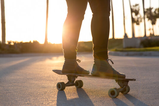 Low section of woman standing on skateboard during sunset